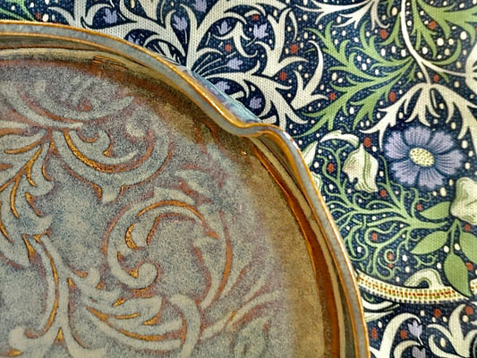 close-up of a beige ceramic plate with intricate orange scrollwork on floral patterned fabric background