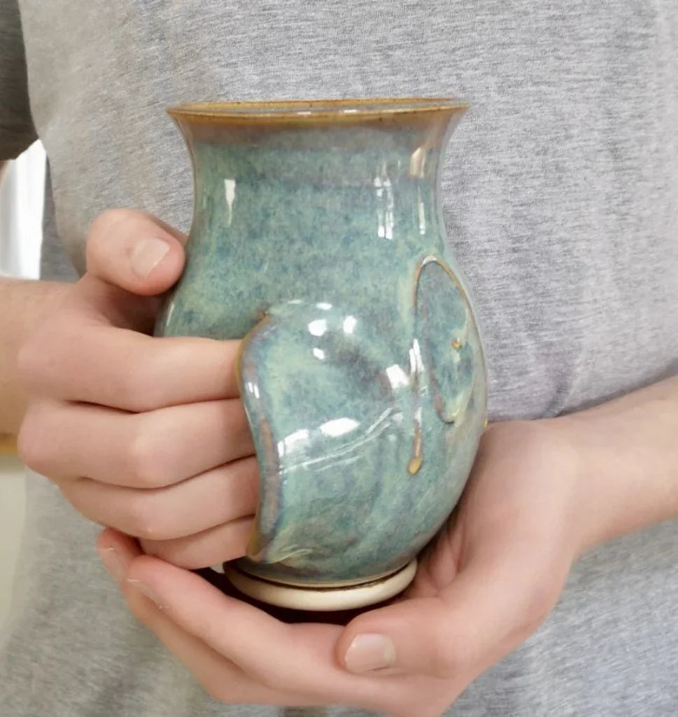 Handcrafted ceramic hanwarmer mug in green glaze held by person in grey shirt, Kilkenny pottery