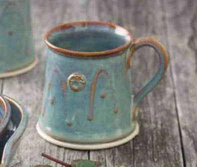 Handcrafted blue ceramic mug with rustic brown rim and embossed design on wooden surface