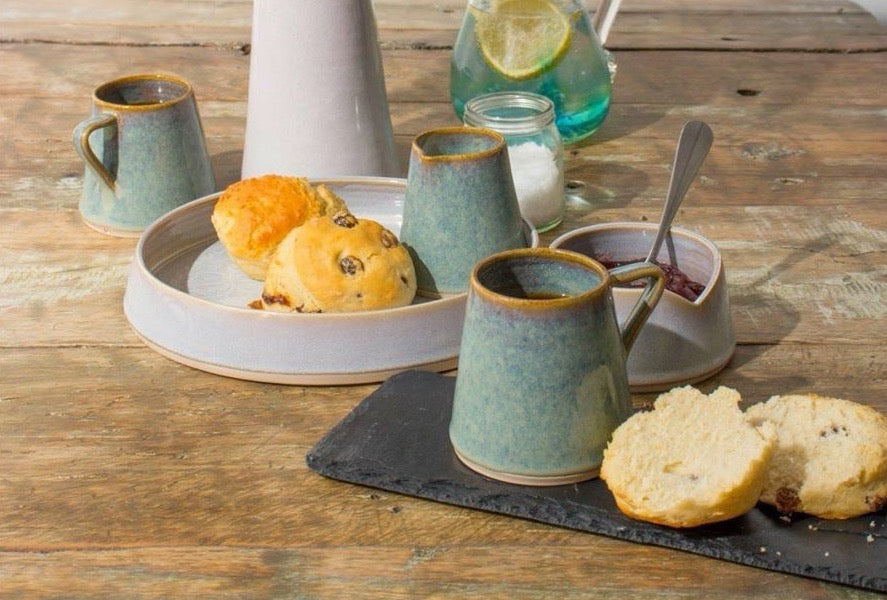 White serving dish with wavy edge and pattern, mugs and creamer with scones and jam on a wooden table.made by castle arch pottery