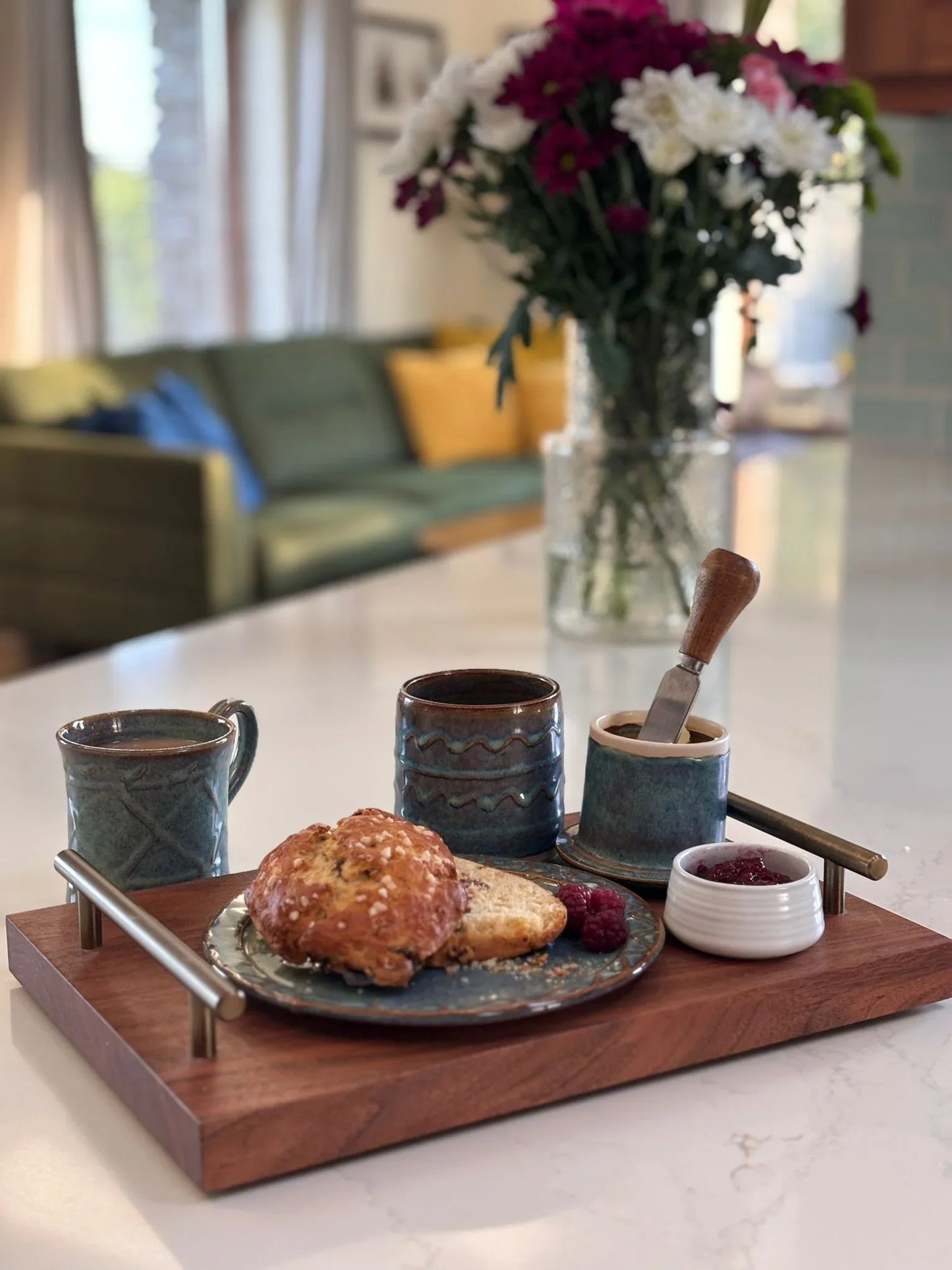 Handcrafted Kilkenny pottery set including mugs, butter crock with knife, jam pot, and plate with scones and raspberries on wooden tray