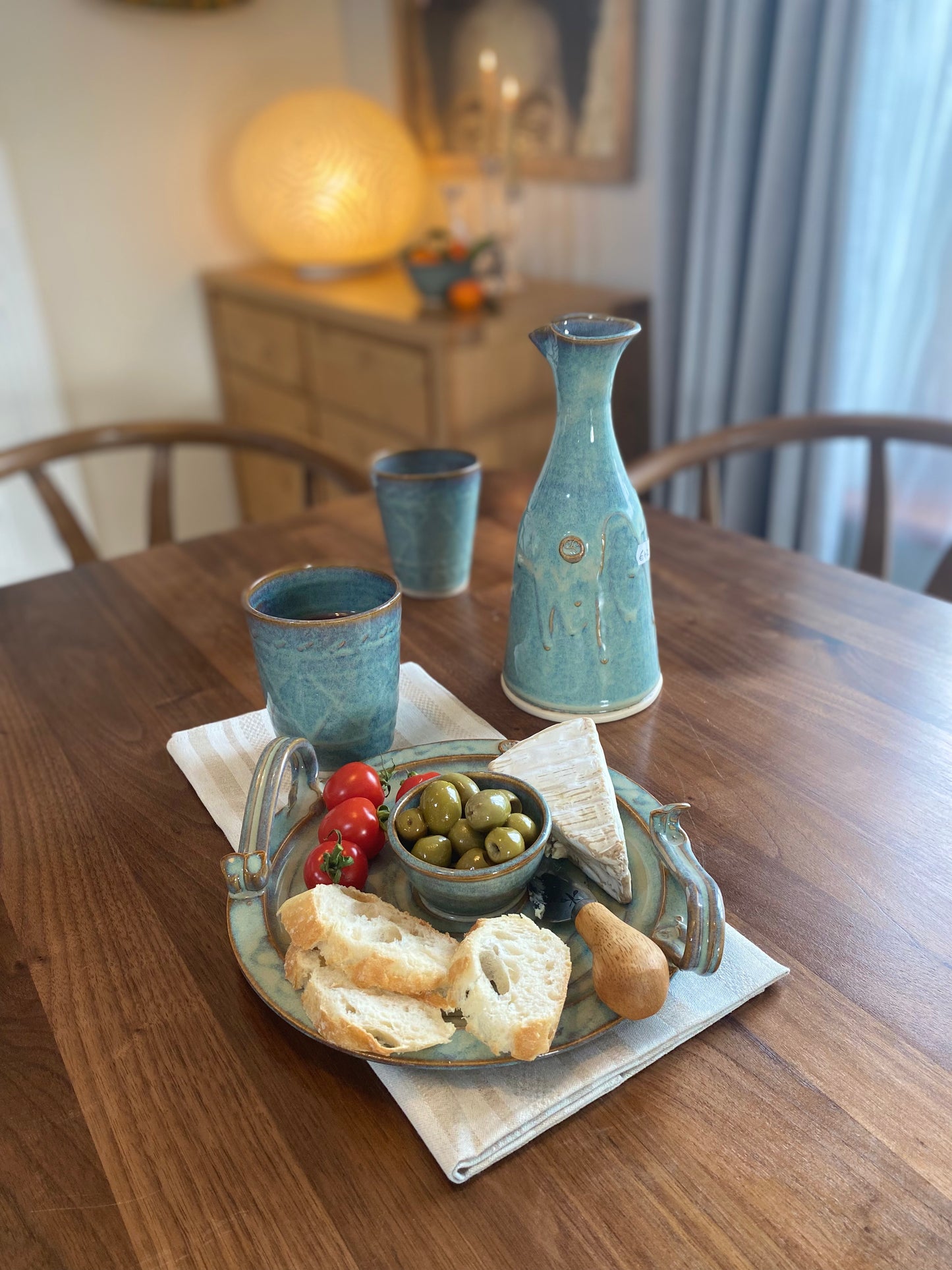 Kilkenny pottery set with ceramic carafe, two cups, and tray holding olives, bread, cherry tomatoes, and cheese on wooden table