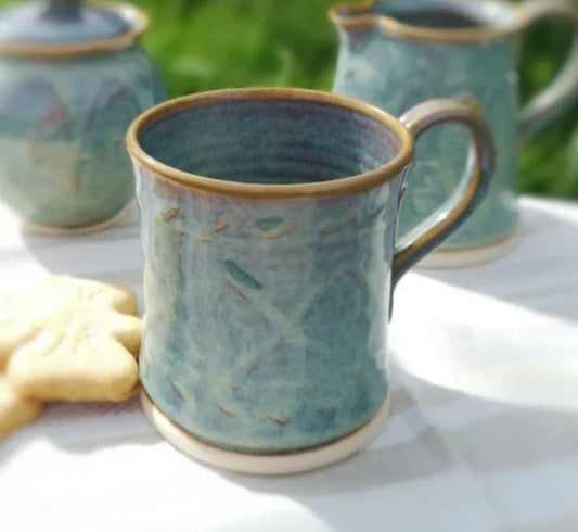 Handcrafted Kilkenny pottery blue ceramic mug with textured surface on white table with cookies