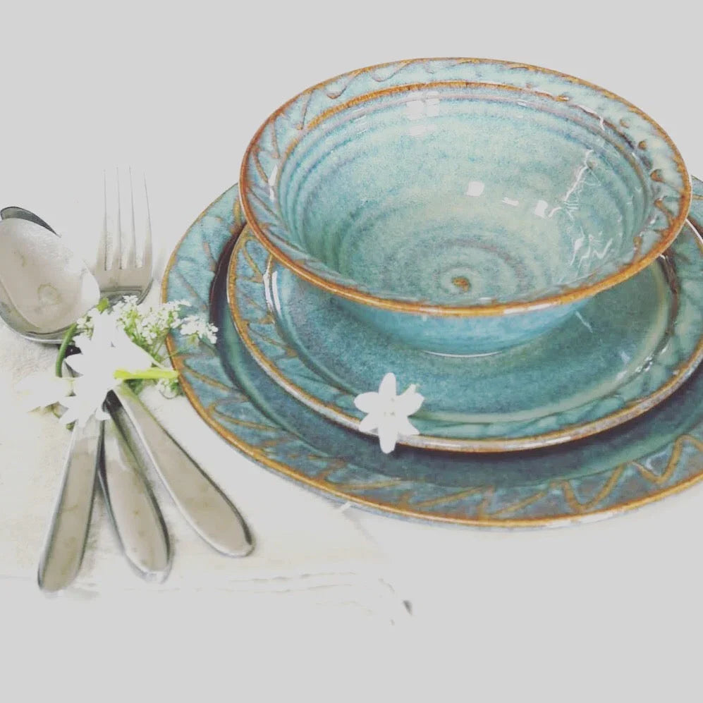 Handcrafted blue ceramic bowl and plates with intricate patterns, accompanied by silver cutlery and white flowers